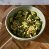 Bowl of cucumber salad with chopped peanuts and herbs on a wooden table.